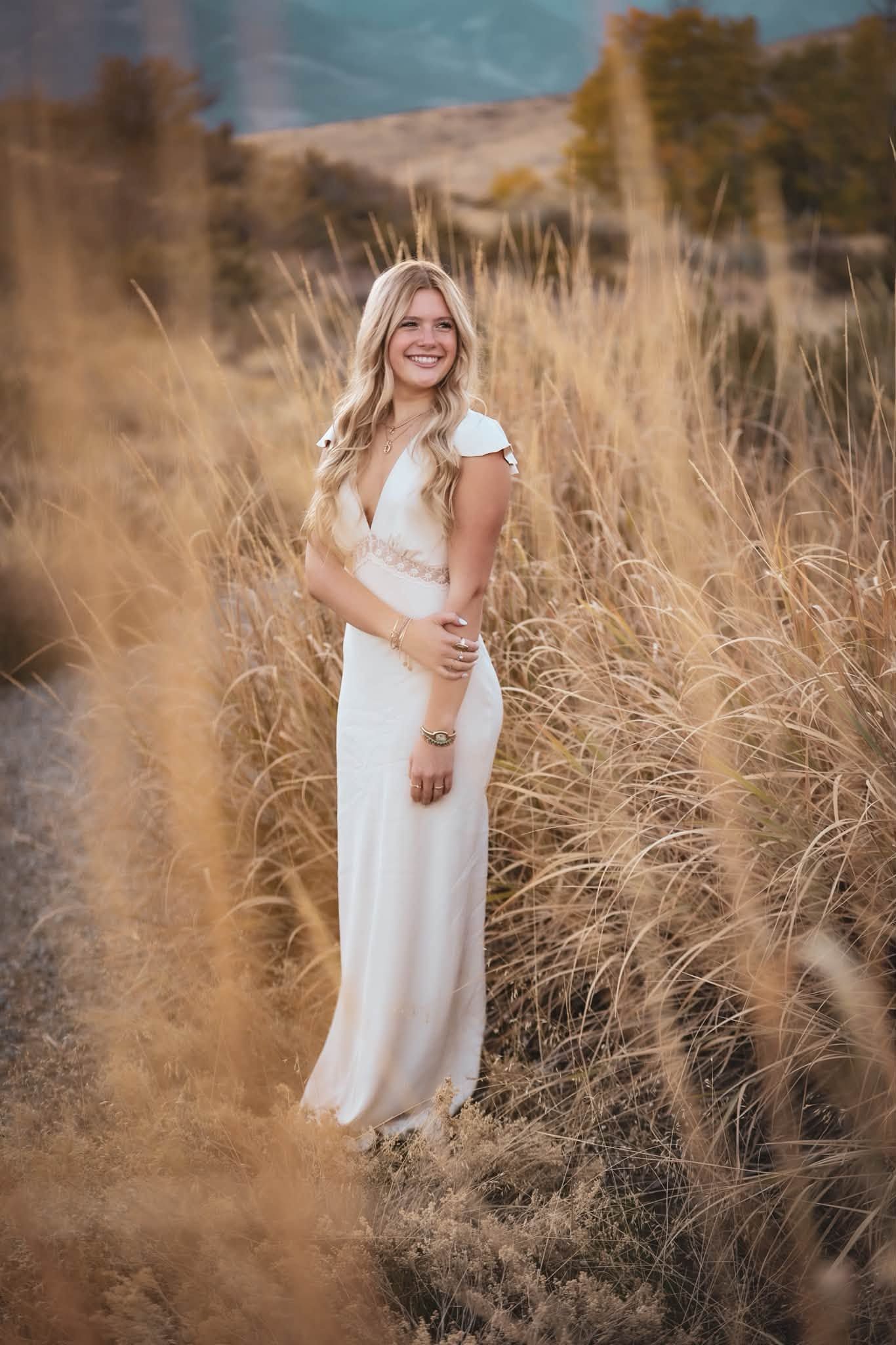 A woman in a flowing white dress standing in tall golden grass at sunset